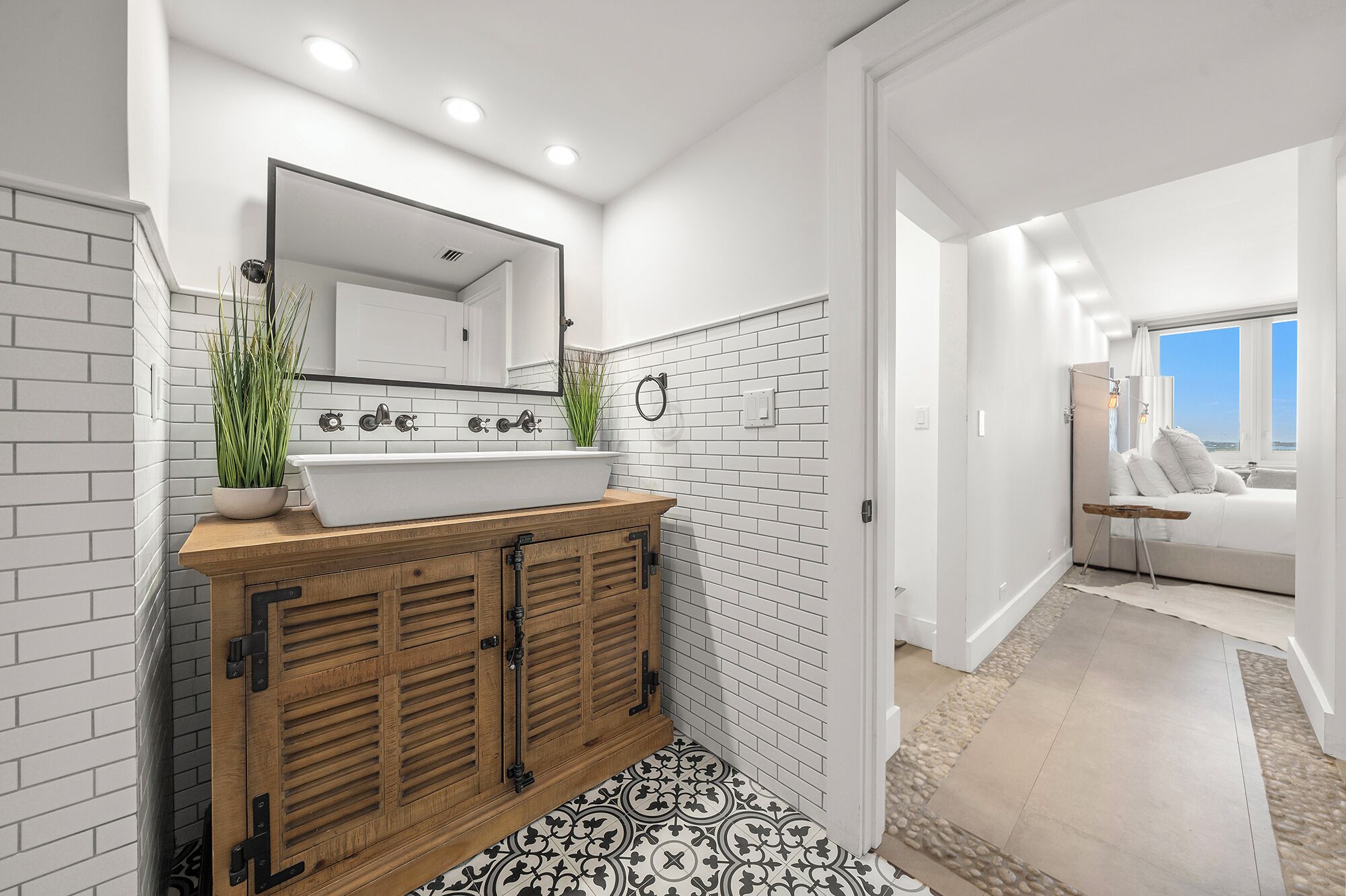 A modern bathroom with a white subway tile backsplash, a wooden vanity, a large mirror, and a potted plant.