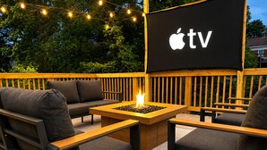 Ulkoterassi, jossa on nuotiopaikka, televisioruutu, jossa näkyy Applen TV-logo, ja puinen lattiapinta.