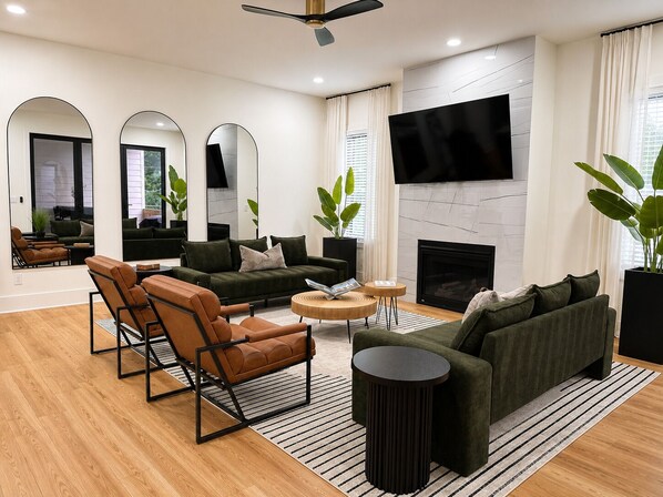 A modern living room with a sofa, chairs, a coffee table, a fireplace, and a TV. - NEW! The Dwelling Place w/ Rooftop Theater, Fire Pit, Game Room near World Cup (Atlanta)