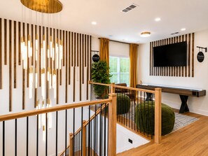A modern interior with a wooden staircase, a flat-screen TV, and a decorative wall panel. - NEW! The Dwelling Place w/ Rooftop Theater, Fire Pit, Game Room near World Cup (Atlanta)