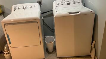 Deux machines à laver à chargement frontal, de couleur blanche, sont placées dans un coin, à côté d’une petite poubelle et d’un seau blanc.