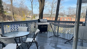Une terrasse extérieure couverte, équipée d’un barbecue, d’une table ronde avec des chaises et d’un hamac.