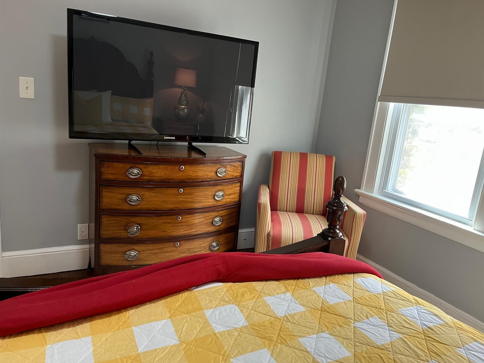 A bedroom with a bed, a dresser, a chair, a television, and a window.