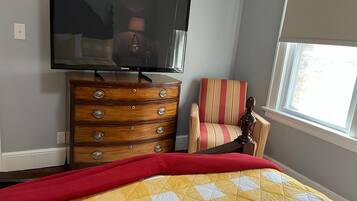 A bedroom with a bed, a dresser, a chair, a television, and a window.