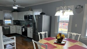 Une cuisine avec des meubles blancs, des appareils en acier inoxydable, une table à manger avec des chaises et une fenêtre donnant sur un immeuble.