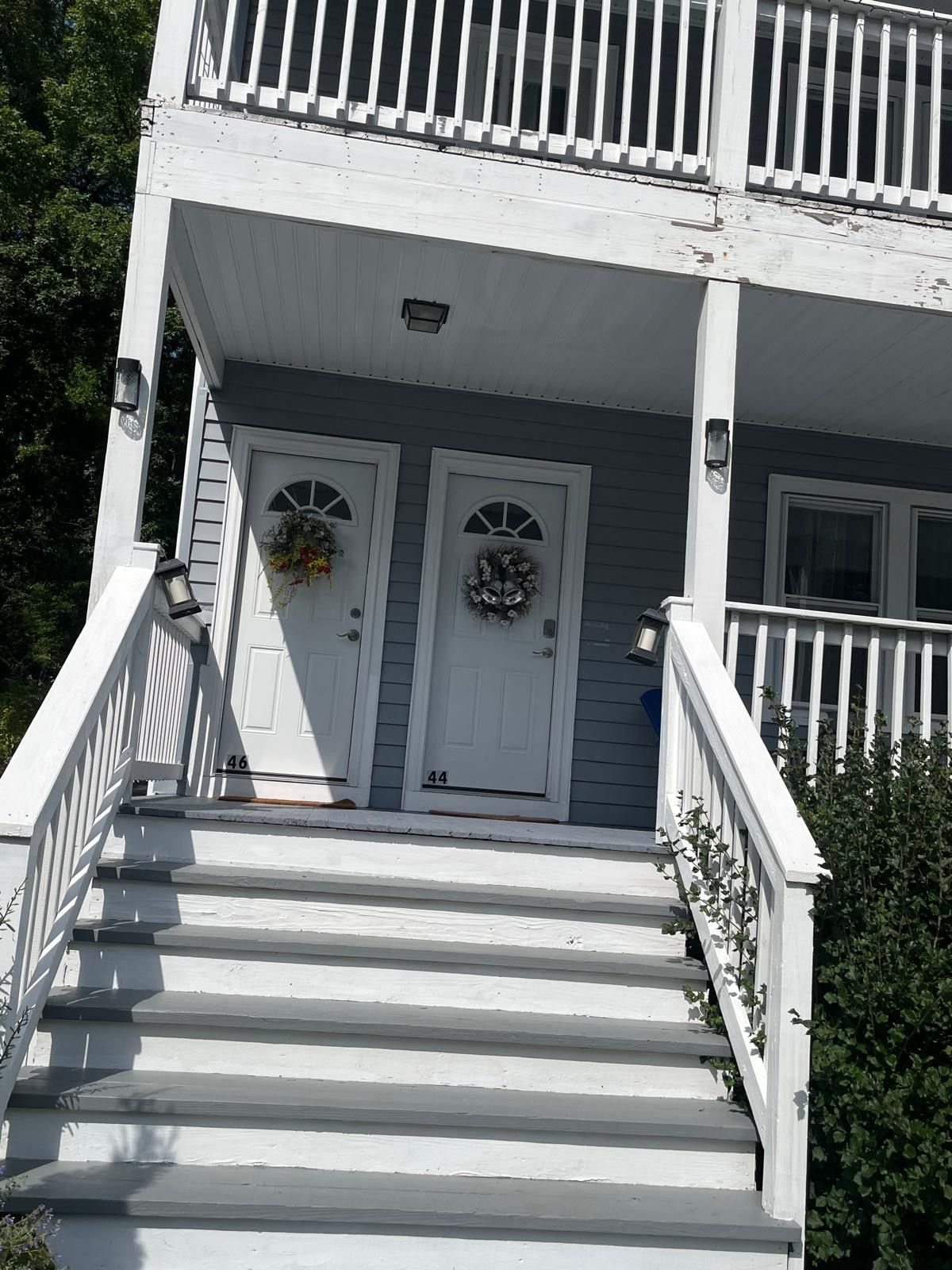 A two-story house with a white exterior, a front porch with steps, and two doors with numbers 46 and 44.