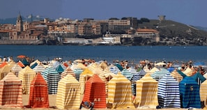 A beach with striped beach umbrellas and a cityscape in the background. - Apartamento en Calafell Cerca de la Playa (Calafell)