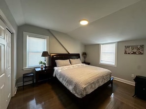 A bedroom with a bed, two nightstands, a ceiling light, and a window with blinds.