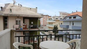 A balcony with a round table and chairs, a satellite dish, and a view of neighboring buildings. - RG007 - Bellaria, comfortable three-room apartment 100 meters from the sea (Bellaria-Igea Marina)