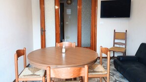 A round wooden dining table with chairs, a black sofa, a television mounted on the wall, and a door with frosted glass panels. - RG007 - Bellaria, comfortable three-room apartment 100 meters from the sea (Bellaria-Igea Marina)