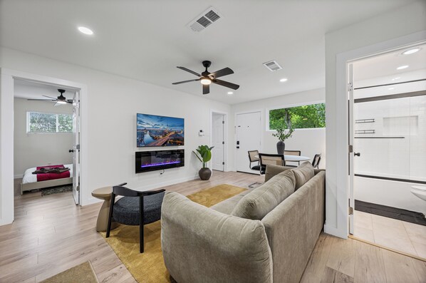Un salon moderne comprenant un canapé, un téléviseur, un ventilateur de plafond et un coin repas avec une table et des chaises.