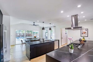 A modern kitchen with a central island, pendant lighting, and a view to the outside. - Wellness Retreat 5BR Villa w/ Pool, Sauna, hot tub (Austin)