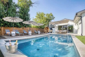 A swimming pool with lounge chairs and umbrellas, a wooden deck, and a glass-enclosed area. - Wellness Retreat 5BR Villa w/ Pool, Sauna, hot tub (Austin)