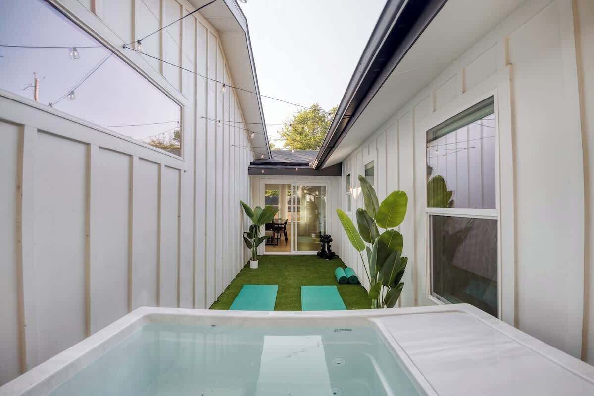 A narrow outdoor space with a hot tub, green artificial turf, and potted plants.