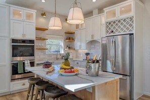 A modern kitchen with white cabinetry, stainless steel appliances, and a central island with stools. - 7BR Estate, Heated Pool, Hot Tub, Cabana Theater (Austin)