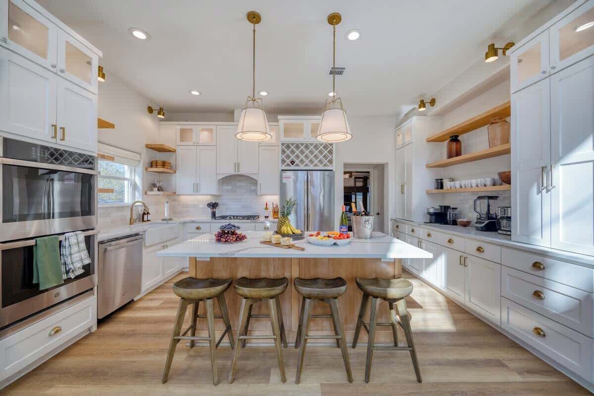 A modern kitchen with white cabinetry, a central island with stools, stainless steel appliances, and pendant lighting.