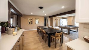 Un comedor amplio con una mesa de billar, sillas de madera y una mesa larga.