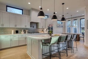 A modern kitchen with white cabinets, a central island with bar stools, pendant lighting, and a large window.