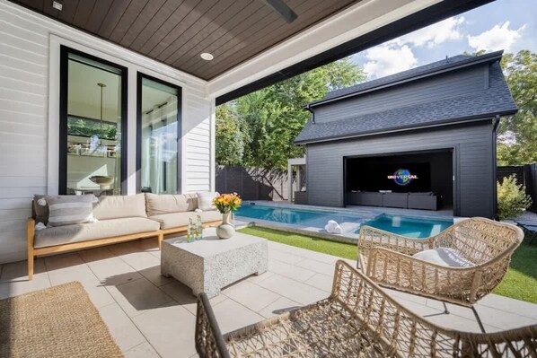 A modern outdoor living area with a pool, a sofa, and a television.