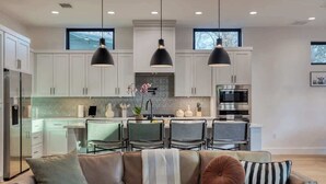 A modern kitchen with white cabinets, a dining area with chairs, and pendant lighting. - Amenities! Pool, Hot Tub, Theater, Outdoor kitchen (Austin)