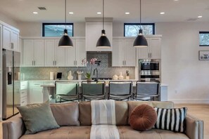 A modern kitchen with white cabinets, a dining area with chairs, and pendant lighting. - Amenities! Pool, Hot Tub, Theater, Outdoor kitchen (Austin)