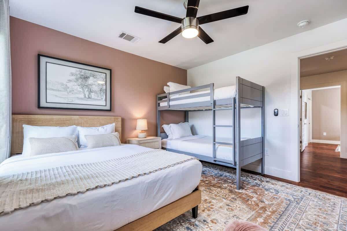 A bedroom with a bed, a bunk bed, a ceiling fan, a nightstand, a lamp, and a framed picture on the wall.