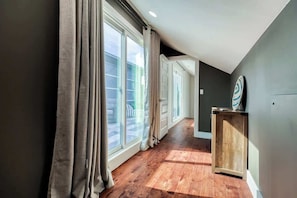 A hallway with large windows, a wooden floor, and a small cabinet with a decorative plate. - Luxury East Austin 6BR | Pool, Hot Tub, Roofdeck (Austin)