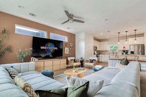 A modern living room with a flat-screen TV, a ceiling fan, and a kitchen in the background. - Luxury East Austin 6BR | Pool, Hot Tub, Roofdeck (Austin)