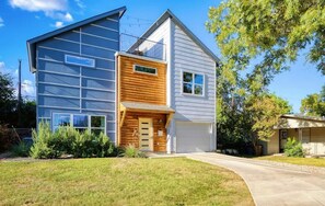 A modern two-story house with a garage, a wooden front door, and a large window. - Luxury East Austin 6BR | Pool, Hot Tub, Roofdeck (Austin)
