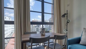 Ein Zimmer mit einem großen Fenster, einem Tisch mit Stühlen, einem blauen Sofa und einer Stehlampe.