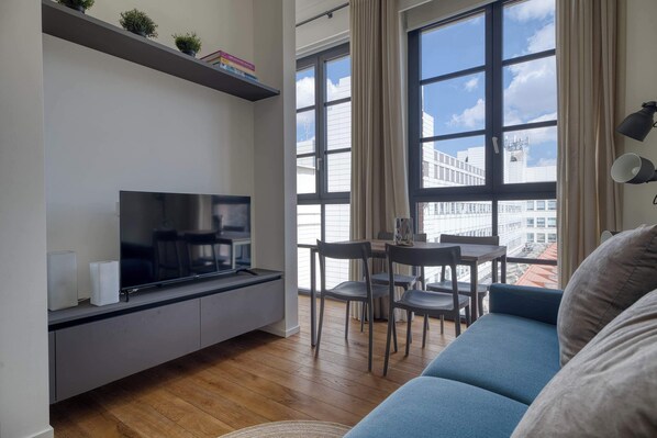 A modern living room with a flat-screen TV, a sofa, a dining table with chairs, and large windows with curtains. - w* | Bright 1BR near to the center of Milan (Milano)
