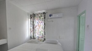 Un dormitorio con cama, ventana con cortinas florales, equipo de aire acondicionado y puerta verde.