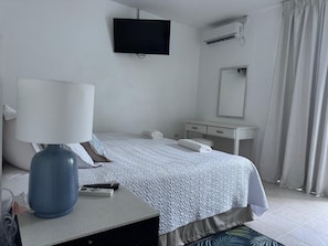 Habitación de hotel con cama, escritorio con lámpara, televisión, espejo y equipo de aire acondicionado.