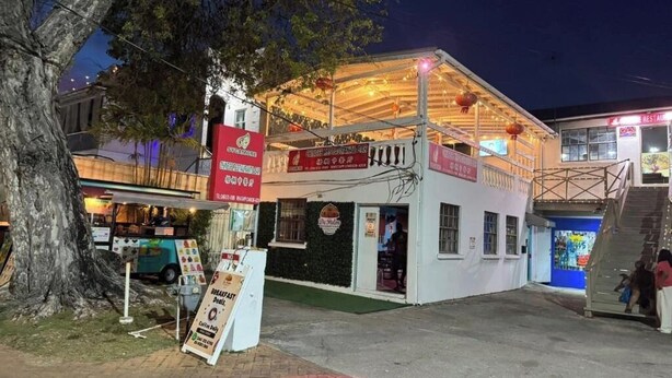 Un camión de comida con un cartel, un edificio pequeño con balcón y una escalera que lleva a un segundo piso.