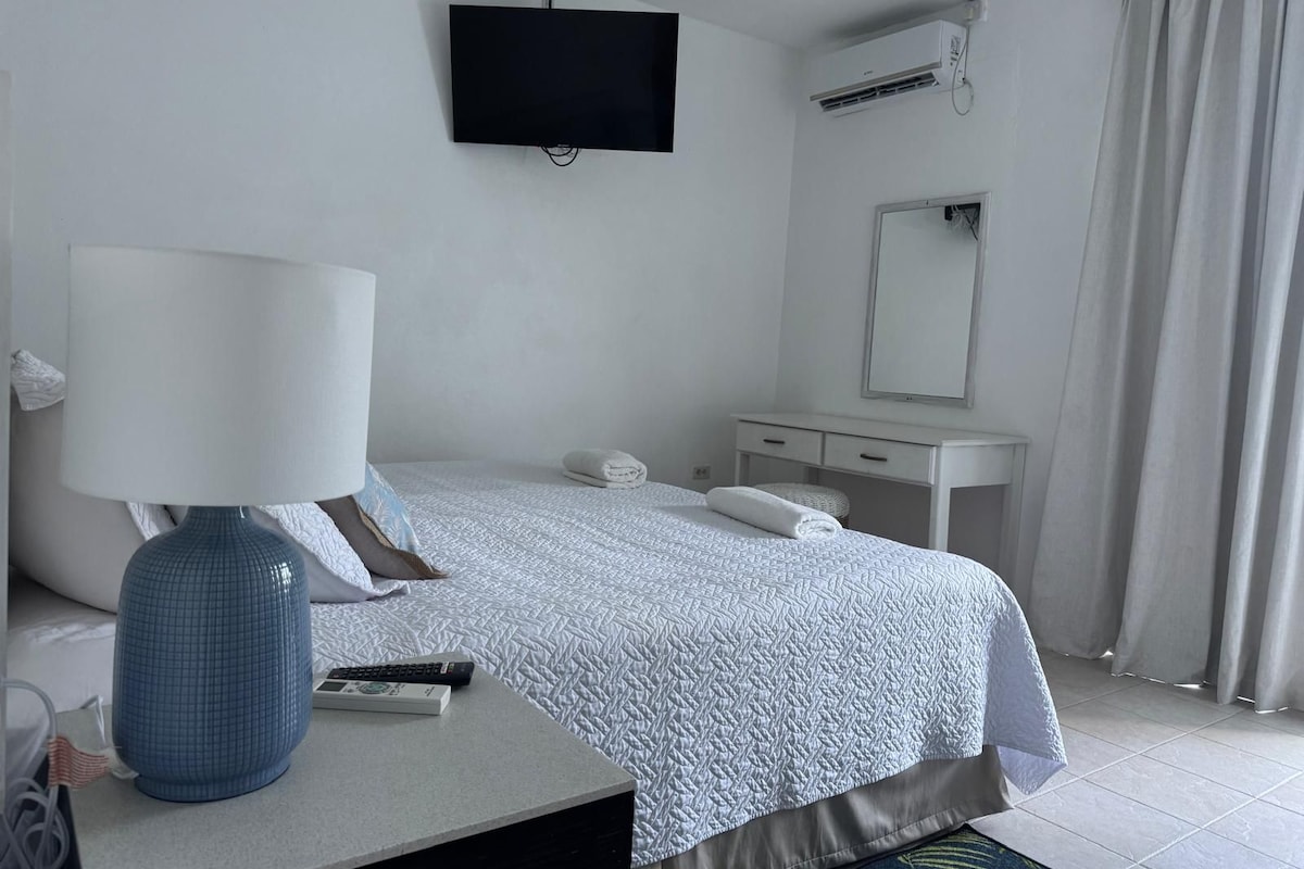 Habitación de hotel con cama, escritorio con lámpara, televisión, espejo y equipo de aire acondicionado.