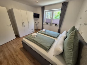 A bedroom with two beds, a wardrobe, a TV, and a window with curtains.
