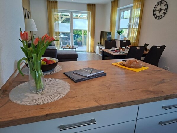 A dining area with a wooden table, a vase of tulips, a bowl of fruit, and a laptop.