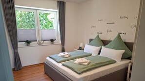 Un letto matrimoniale con biancheria verde e bianca, un comodino con una lampada e una finestra con tende.