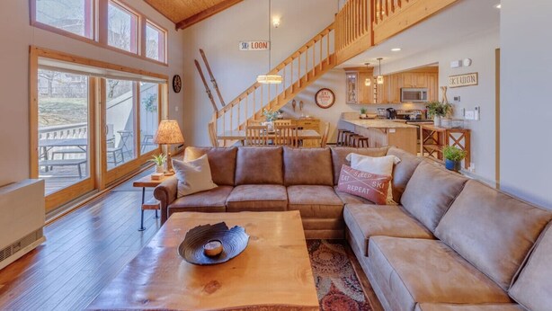 A spacious living room with a large sectional sofa, a wooden coffee table, and a dining area with a staircase. - Stylish and Modern Condo at Loon! Pool & Hot Tub (Lincoln)
