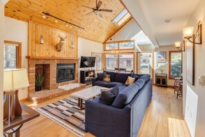 Ein geräumiges Wohnzimmer mit Kamin, einer großen Couch und einem Deckenventilator.