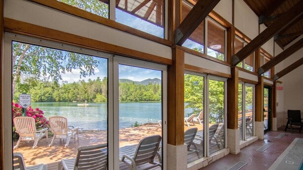 A covered deck with large windows overlooking a lake, chairs, and a pool area. - Deer Park End Unit with Lake Access (Woodstock)