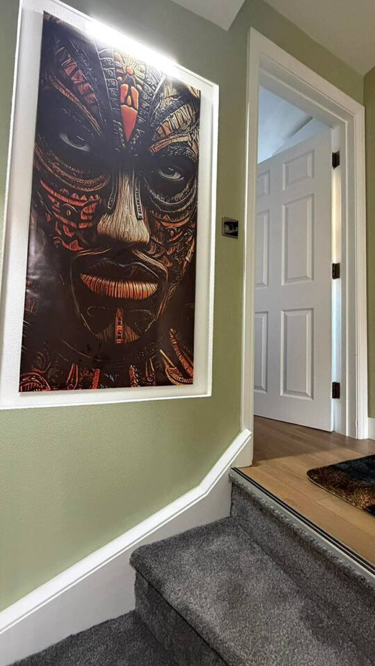 Un pasillo con una escalera, una obra de arte enmarcada en la pared y una puerta al final.