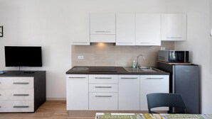 Una cocina compacta con armarios blancos, microondas, pileta y televisión.