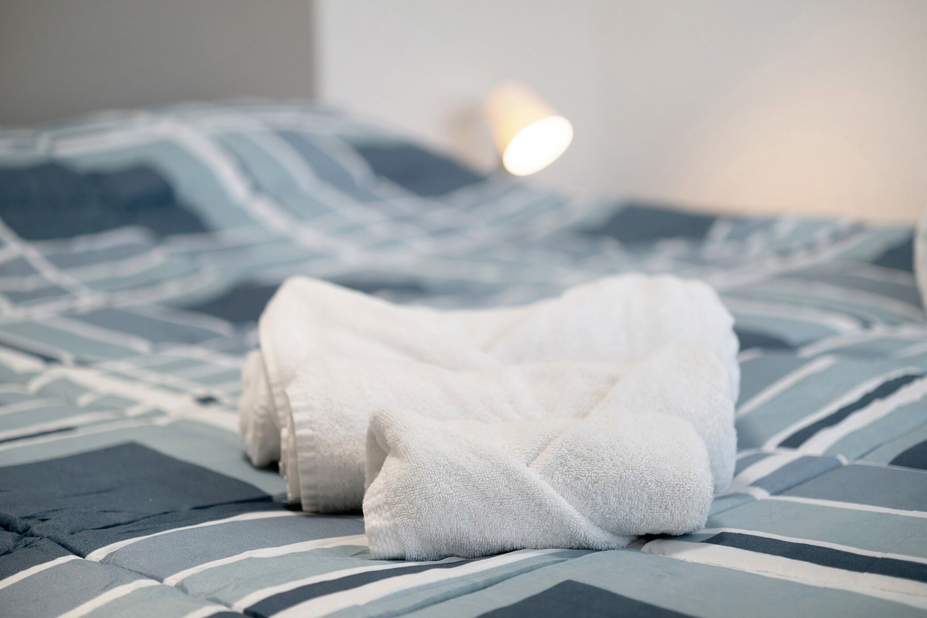 Un lit avec une literie à rayures bleues et blanches, une serviette blanche et une lampe fixée au mur.