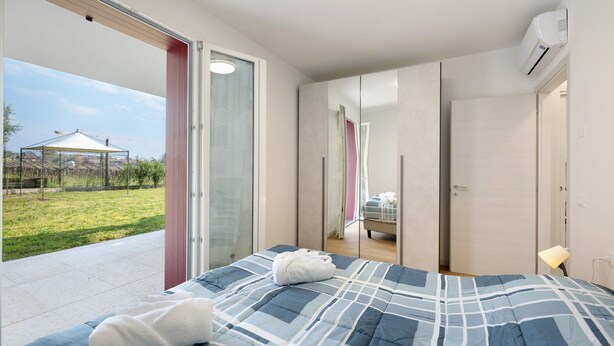 Un dormitorio con cama, un baño con espejo y un cristalero corredizo que da a un espacio exterior.