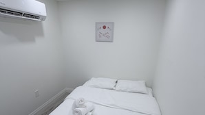 Une pièce propre et blanche, avec un lit, un climatiseur fixé au mur et un petit objet décoratif.