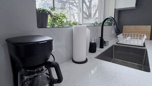 Une cuisine moderne équipée d’une machine à café, d’un évier et d’une fenêtre donnant sur les arbres.