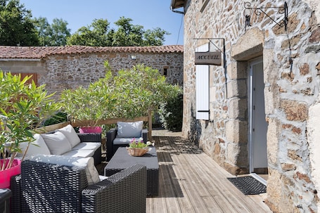 A stone building with a sign reading 'ACCUEIL' and a wooden deck with wicker furniture and potted plants.. Eugénie - Aux Charmes d’Antan Guest Room with Shared Pool, Terrace & Wi-Fi