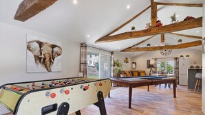 Una habitación con mesa de fútbol, mesa de billar, vigas de madera y un cuadro grande de un elefante.