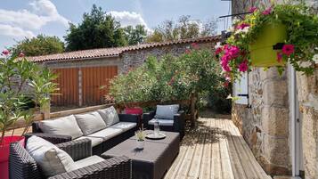 Een terras met rieten meubels, een stenen muur en bloeiende planten.